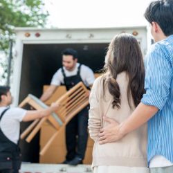 Caucasian delivery man worker delivering package to young couple in house. Attractive courier employee working and deliver box cardboard from car truck infront of new house of new marriage partner.