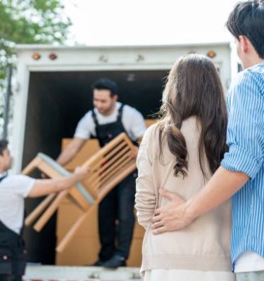 Caucasian delivery man worker delivering package to young couple in house. Attractive courier employee working and deliver box cardboard from car truck infront of new house of new marriage partner.