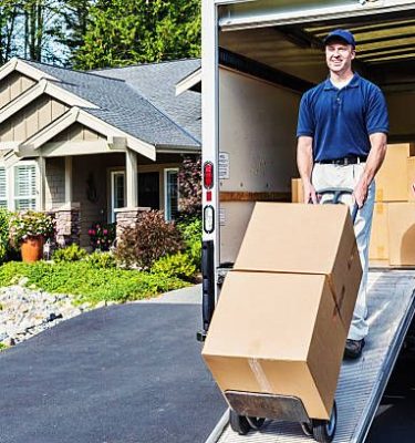 Photo of a delivery man unloading (or loading) truck, walking cardboard boxes down ramp on a hand truck.